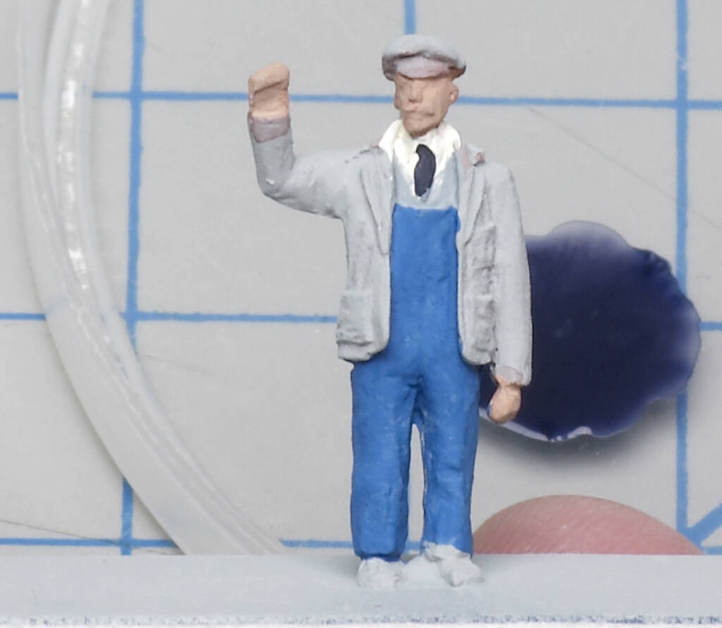 Color photo of scale figure wearing necktie, gray jacket, and blue overalls.