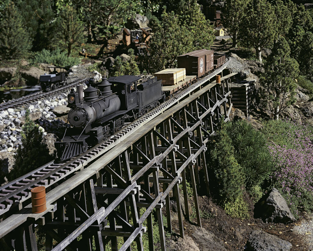 A model steam locomotive on an elevated trestle bridge in an garden railroad