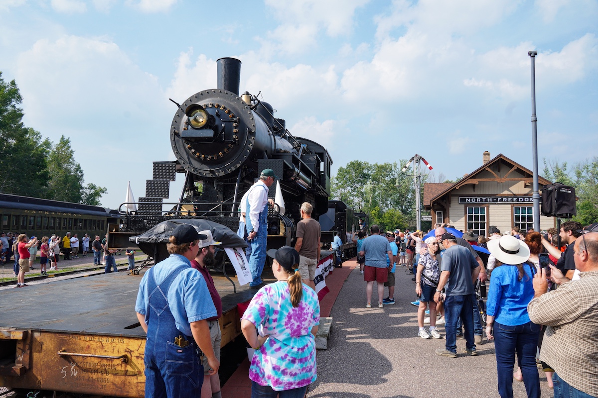 Crowds surround steam locomotive on a flatcar