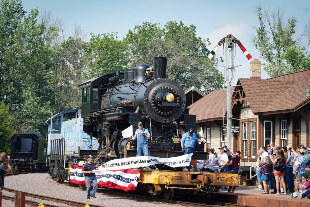 Flat car with steam locomotive on top breaks banner