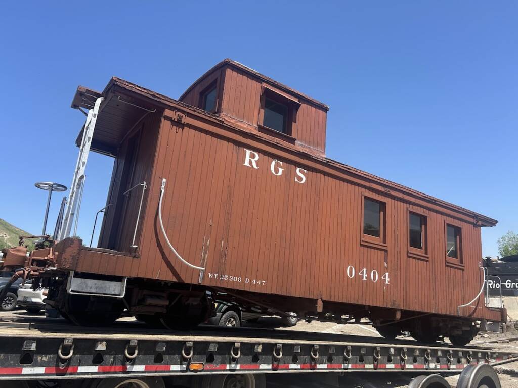 Wooden narrow-gauge caboose loaded on a flatbed