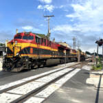 Train with red, yellow, and black locomotives at grade crossing