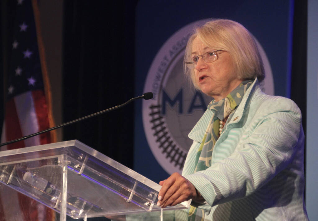 Woman in light green coat speaking at podium