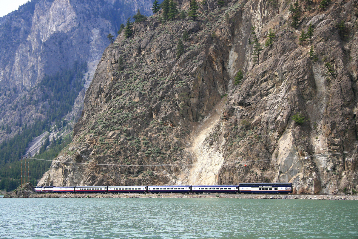 Passenger train running along lake shore next to steep mountainside