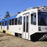 White articulated light rail vehicle with blue and yellow trim