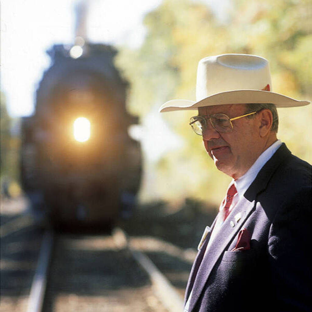 Man in suit and hat with steam locomotive in background