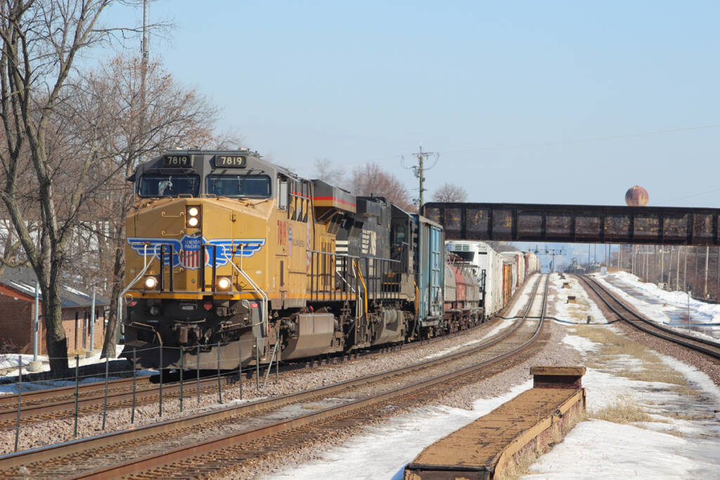 Freight train passes under bridge as it rounds gentle curve on three-track main line.