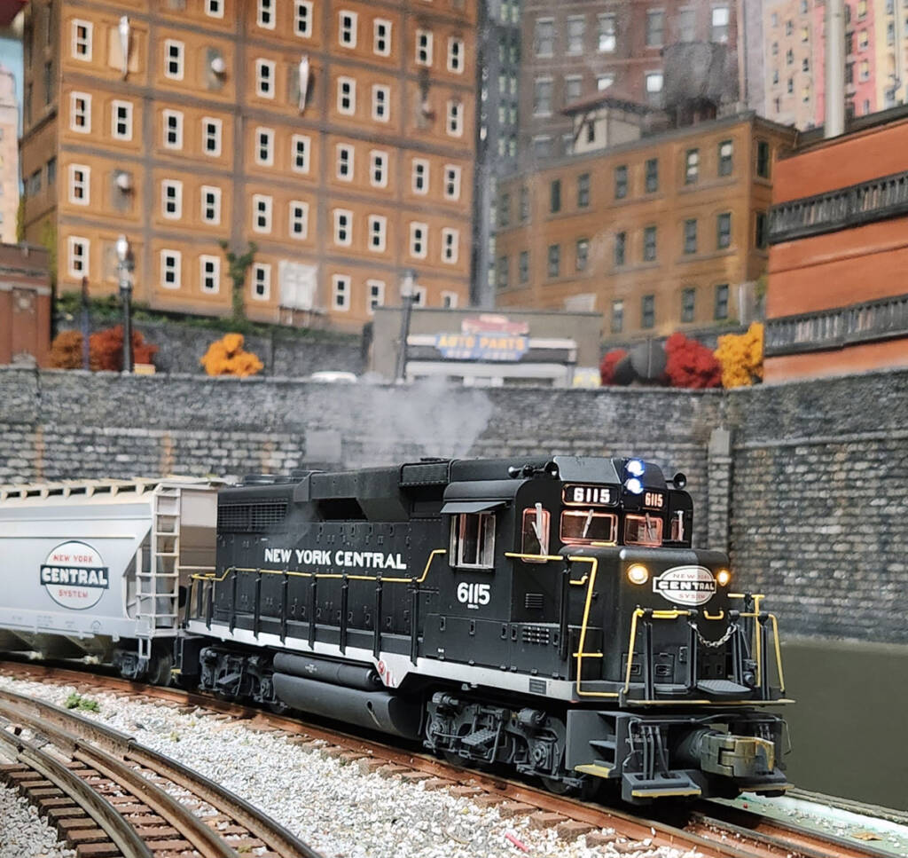 A black toy train locomotive leads a train on a downtown scene