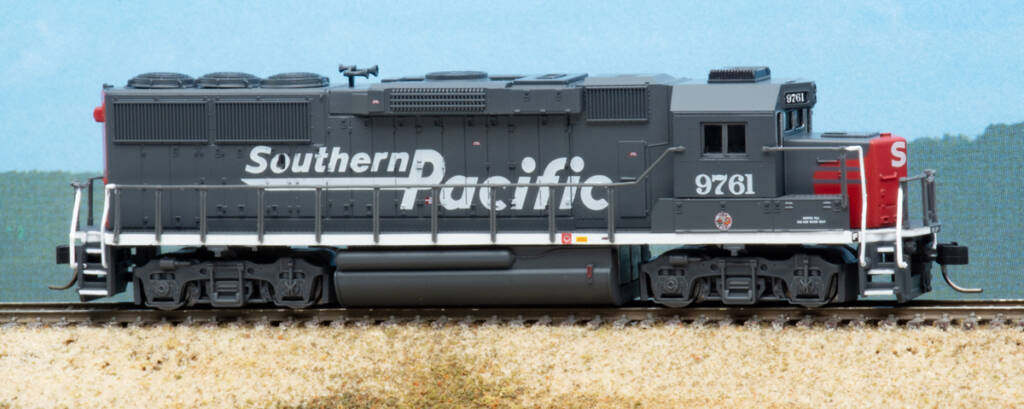 Color photo of N scale hood unit painted gray and red on scenicked base with sky backdrop.
