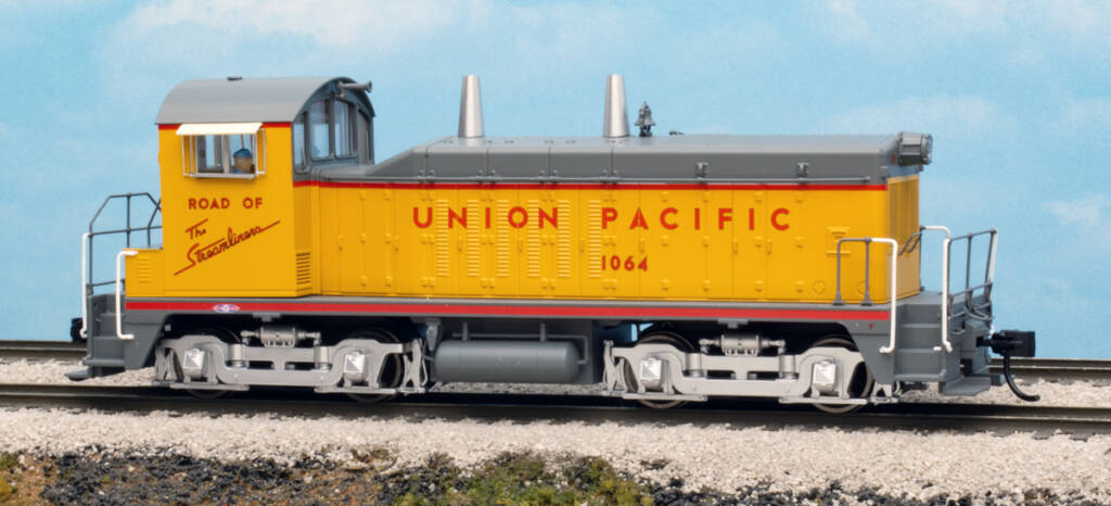 Color photo of HO scale end-cab switcher painted gray, yellow, and silver on scenicked base with sky backdrop. 