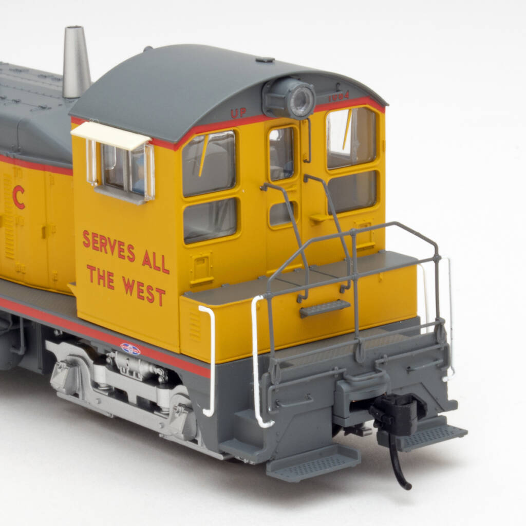 Color photo showing cab end of HO scale switcher. Model is painted yellow, gray, and silver with red graphics and shown on a white background.