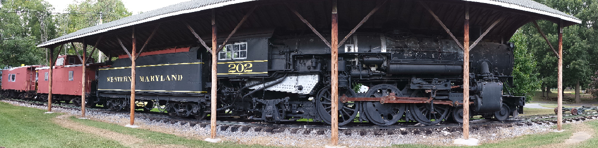 Black steam locomotive under open-air shelter in a park.
