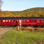 A sideview of a red and black passenger car passing a grade crossing