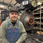 Young individual sitting in front of a narrow gauge steam locomotive