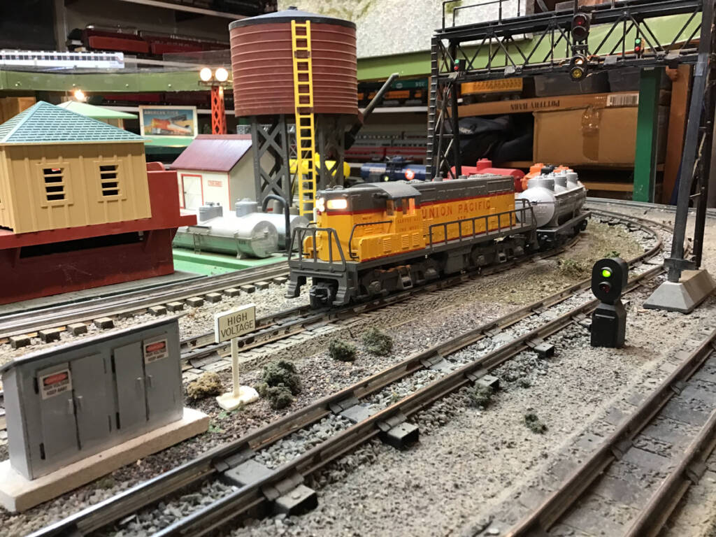 A toy Union Pacific locomotive on a toy train layout leads a freight train with tank cars of various colors