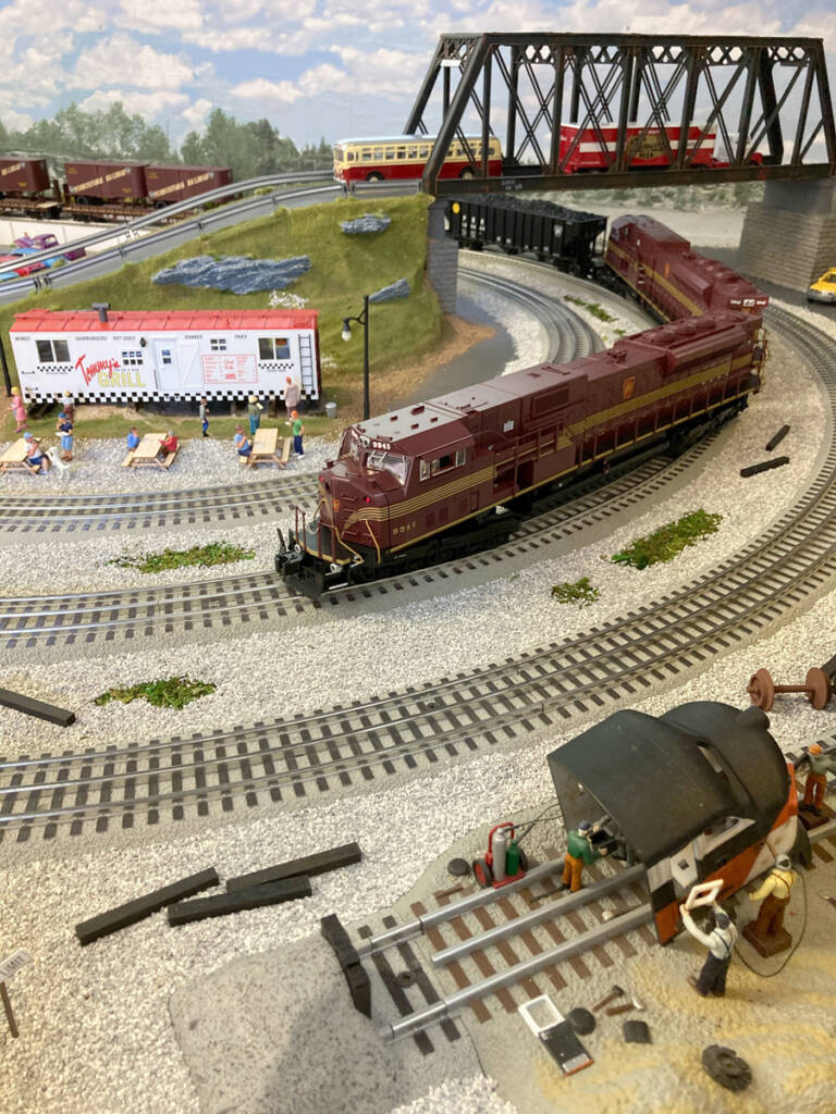 A model train on a model train layout with a bridge in the background of the image