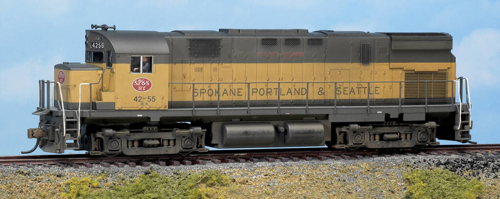 Color photo of HO scale diesel painted yellow and black with red, white, and black graphics on scenic base with sky backdrop.