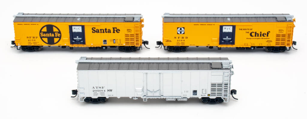 Color photo of three N scale mechanical refrigerator cars, two painted orange and black and one painted silver, all on white background. 