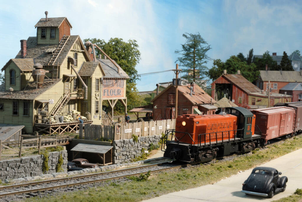 A model train passes a collection of structures on a model railroad layout
