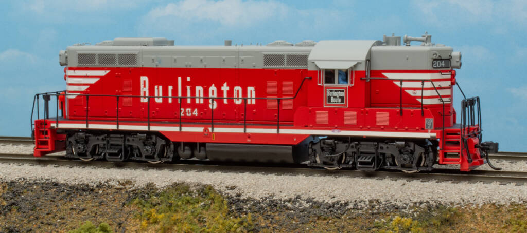 Color photo of HO scale hood unit painted red and gray with red, white, and black graphics on scenic base with sky backdrop.
