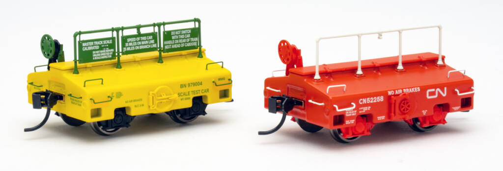 Color photo of two HO scale test cars (one painted green and yellow, one painted orange and white) on white background