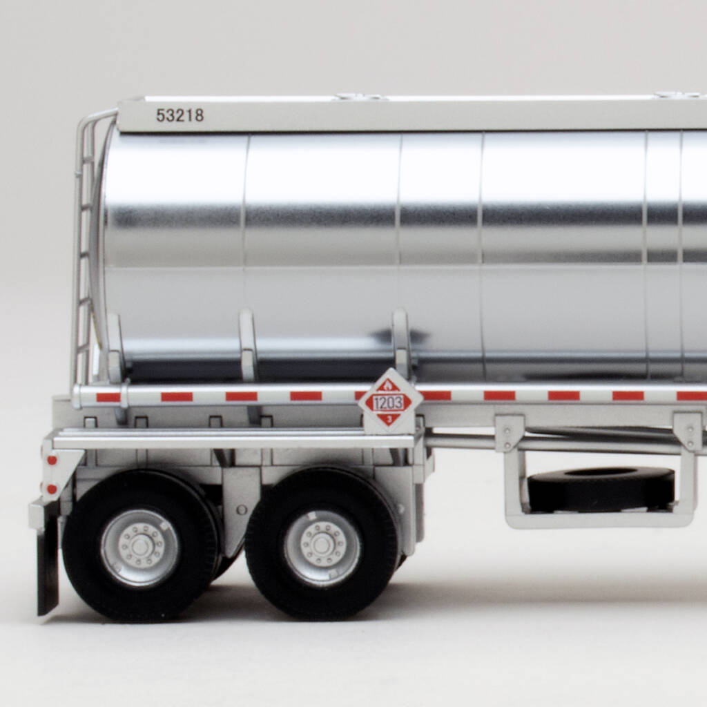 Color photo showing rear side view of HO scale tanker trailer with plated finish, red-and-white stripes, printed hazmat placard, spare tire, and dual rear axles