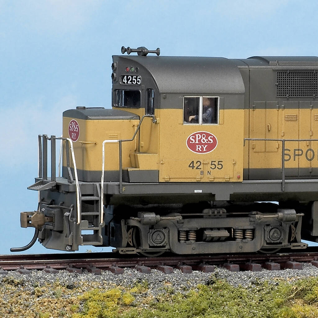 Color photo showing front of HO scale diesel painted yellow and black with red, white, and black graphics on scenic base with sky backdrop.