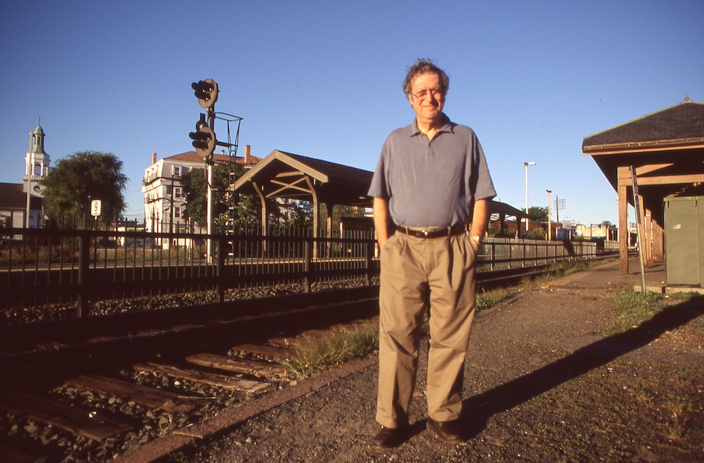 Man standing in front of railroad tracks and a passenger shelter