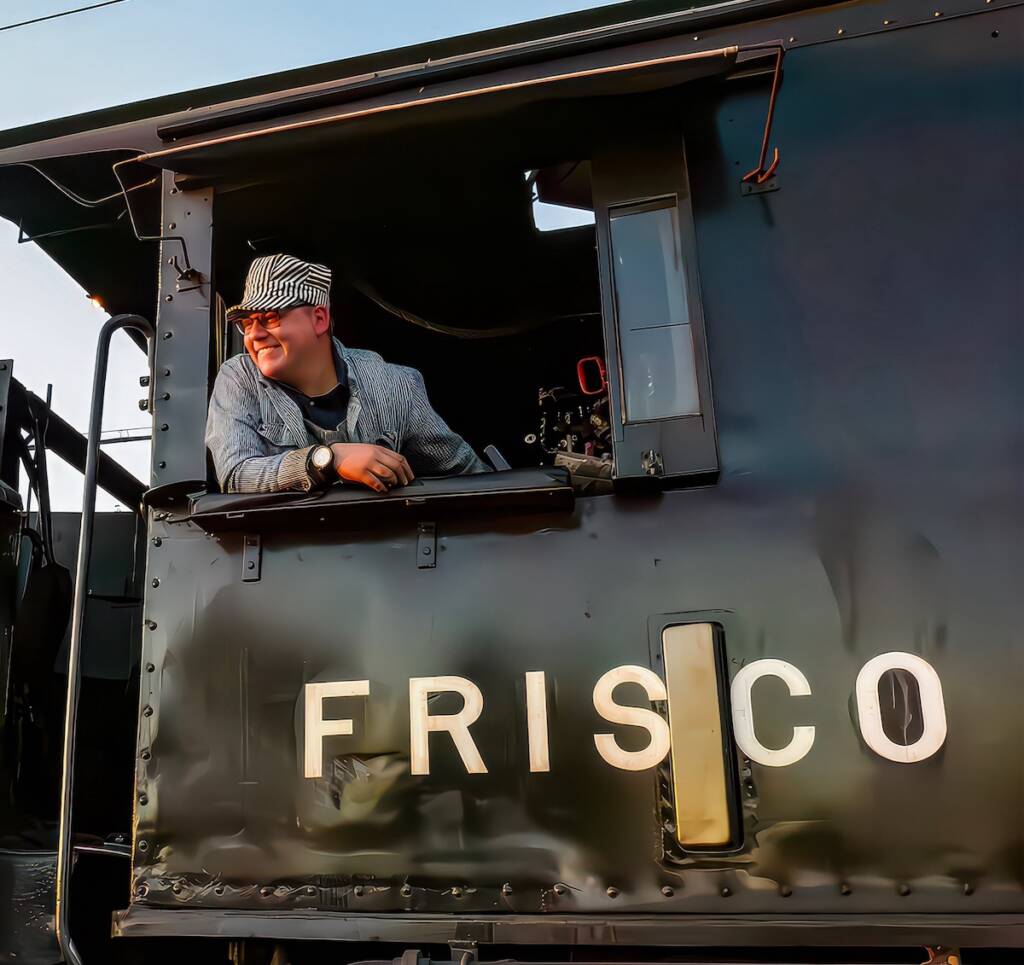 Young individual leaning out of cab of a steam locomotive
