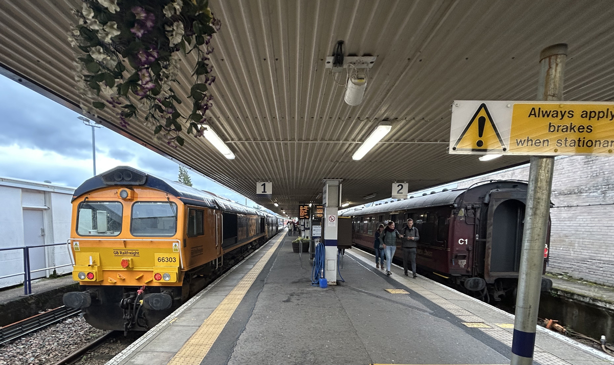 Diesel locomotive on passenger train, and red passenger cars on opposite sides of station platform