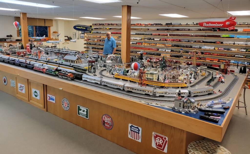 man standing behind large toy train layout