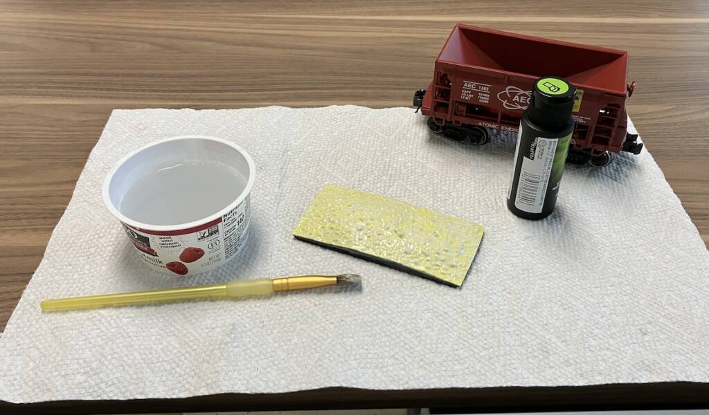 paint brush, cup of water, paint, and parts of model ore car