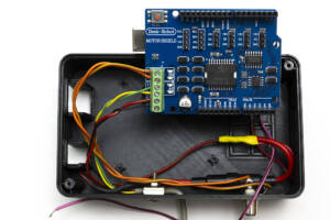 blue motor shield circuit board shown with wiring connections to inside of bottom of case