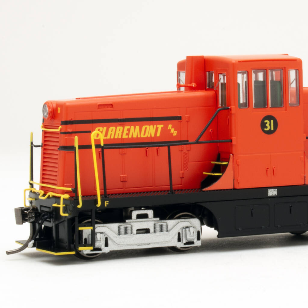 Color photo showing front of HO scale center-cab diesel painted red with yellow and black graphics and silver trucks on white background.