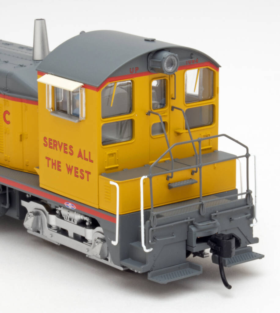 Color photo showing cab of HO scale switcher painted gray and yellow with red graphics on white background.