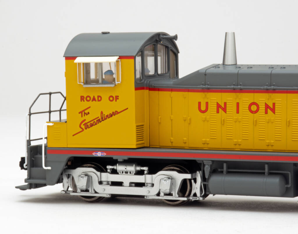 Color photo showing cab and truck on HO scale switcher painted yellow and gray with red graphics on white background.