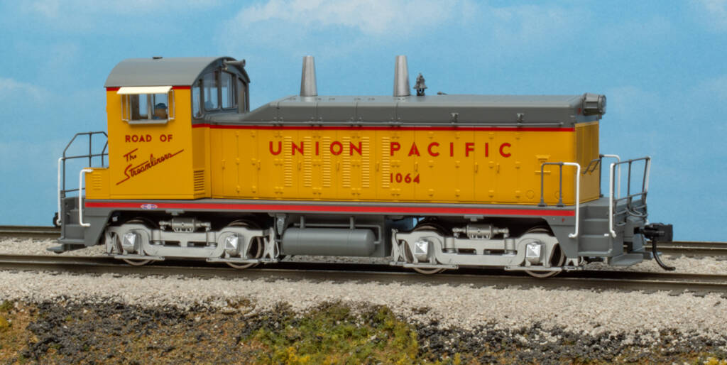 Color photo of HO scale end-cab switcher painted yellow and gray with red graphics on scenicked based with a sky blue backdrop.