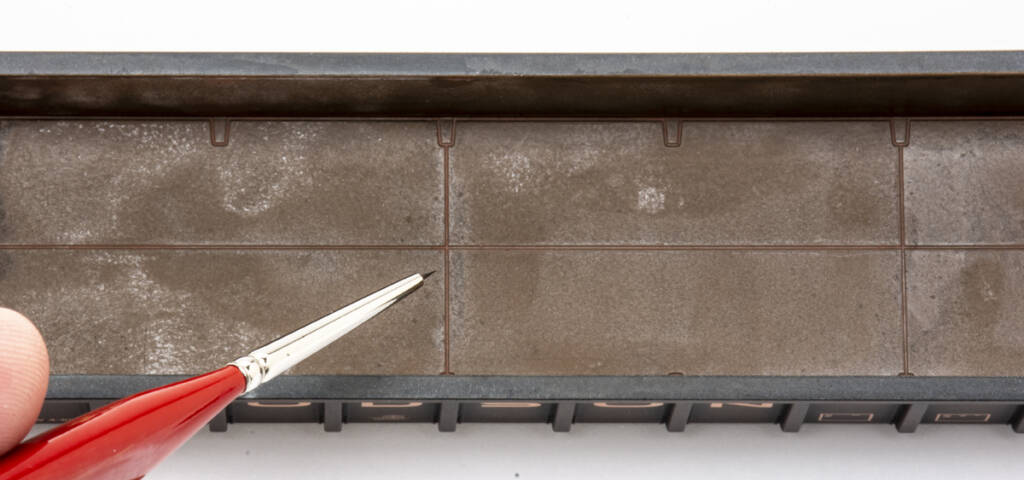 Color photo showing rusty interior of HO scale gondola. At the left edge of the frame is a hand holding a paintbrush with a red handle.