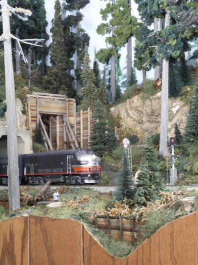 A black and orange streamlined diesel locomotive emerges from a tunnel on the Sunset Valley Oregon System model railroad layout.