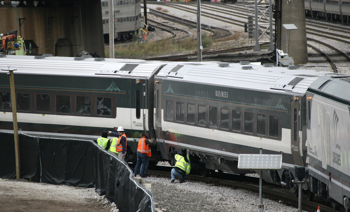 Men in safety apparel looking at wheels and couplers of passenger equipment on tight curve