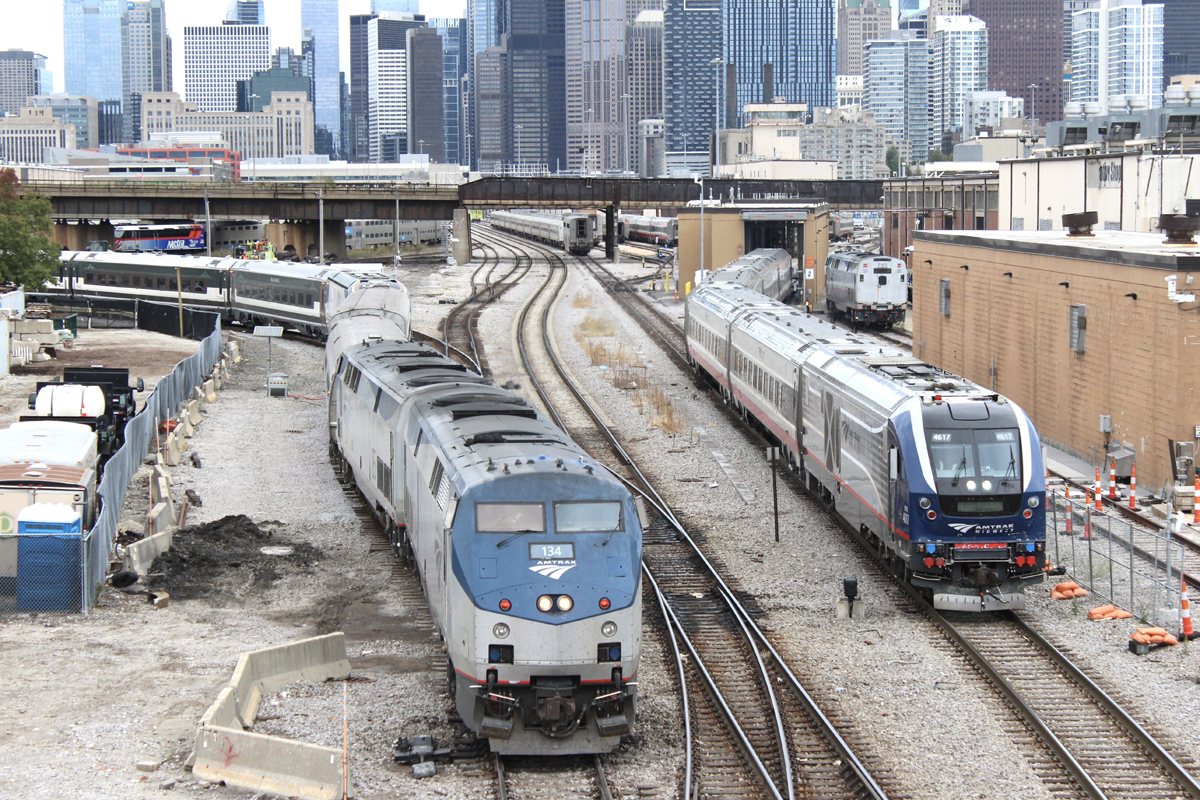 Passenger trains side by side in yard with Chicago skyline in background