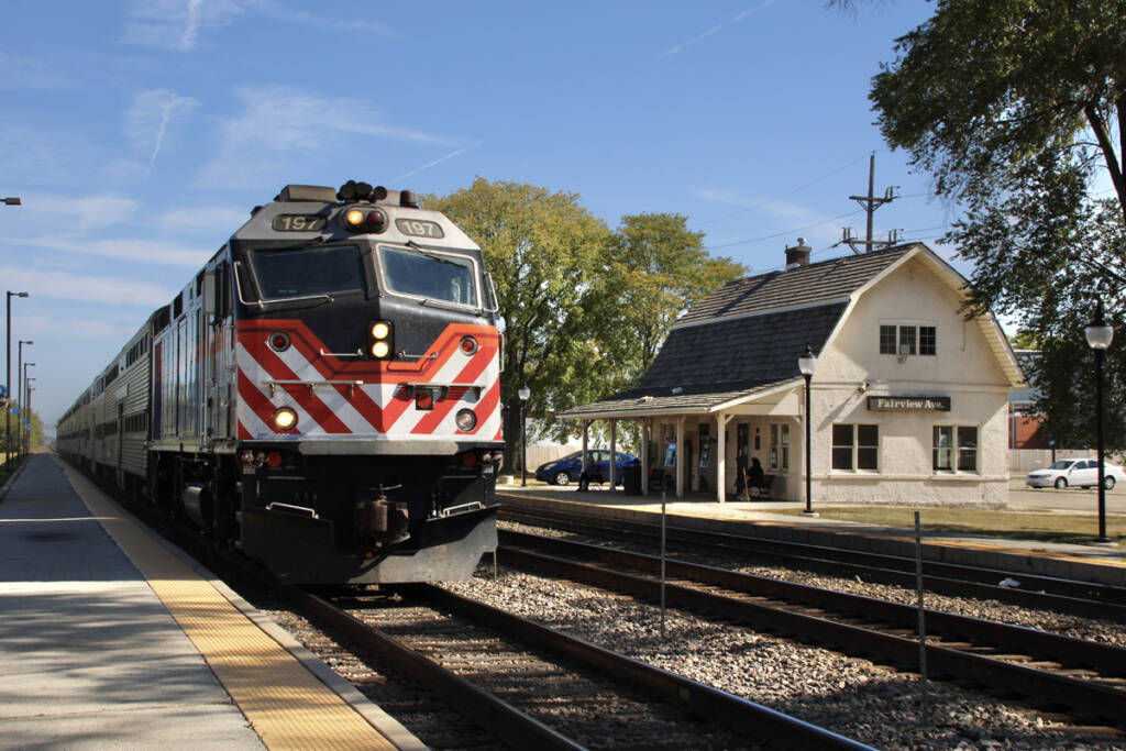 Commuter train stops at platform with barn-like station in background