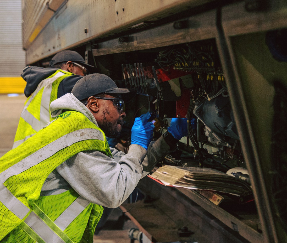 Men in high-visibility safety clothing looking at equipment under commuter railcar