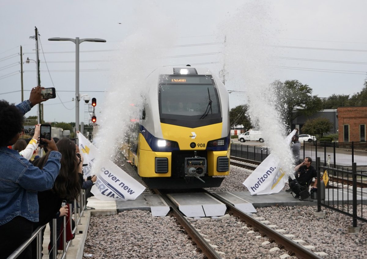 Yellow and white diesel multiple-unit trainset breaks through banner in ceremony