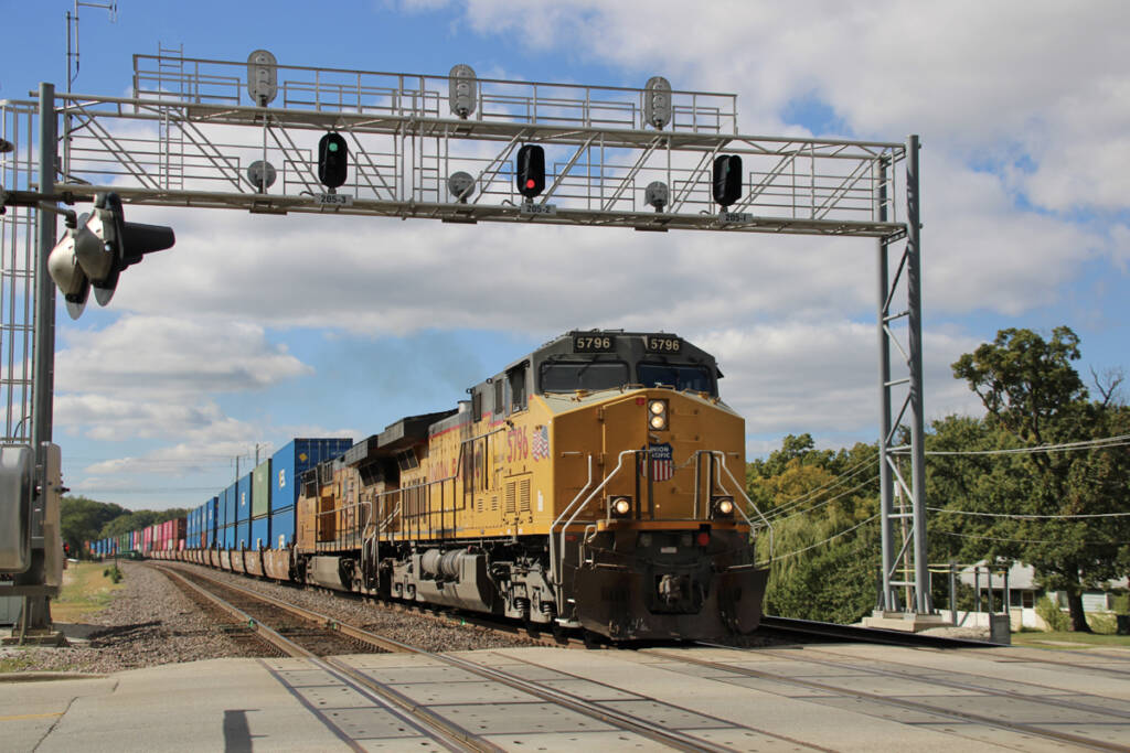 Freight train with two yellow locomotives passing under signal bridge