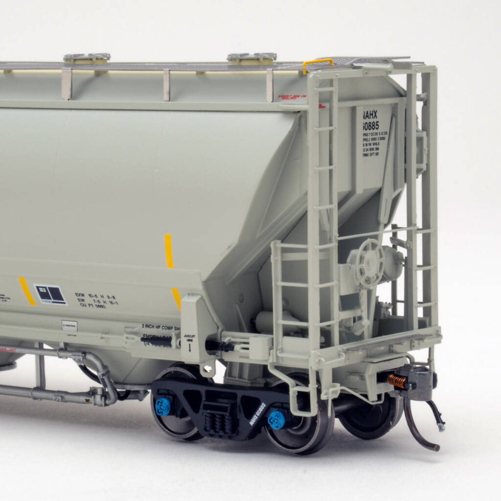 Color photo showing B end of HO scale pressure differential covered hopper painted gray with black lettering; red, yellow, white, and black graphics; and black trucks with blue bearing caps on white background.
