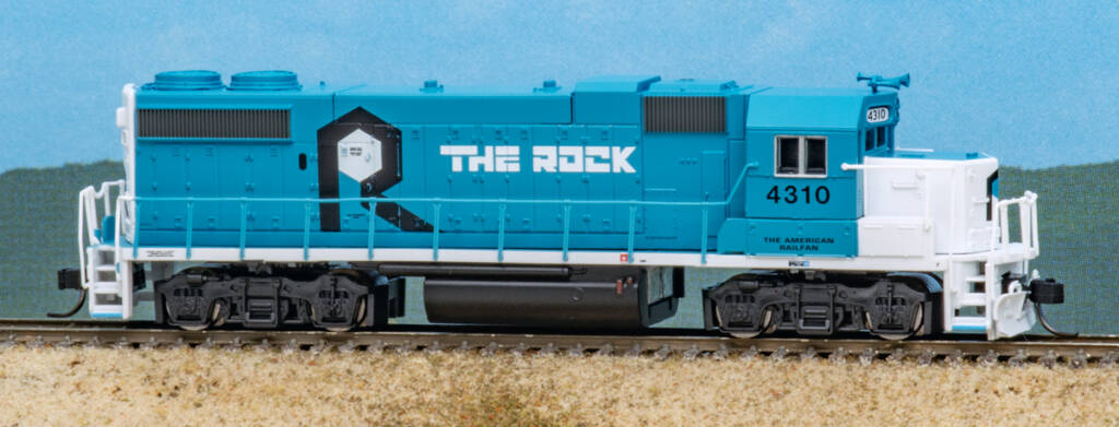 Color photo of N scale hood unit painted blue and white on scenicked base with a sky blue background.