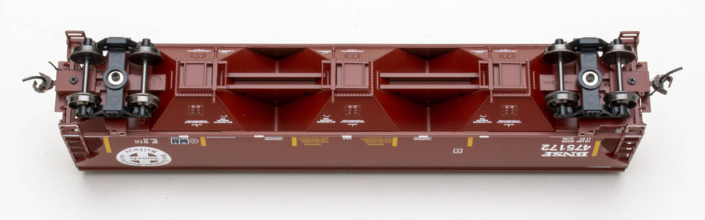 Color photo showing underbody of HO scale three-bay covered hopper painted mineral red with white, yellow, and black graphics on white background.