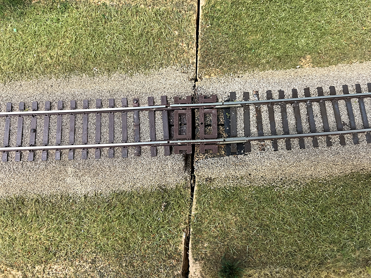 The point where two model railorad layout sections meet, with ballasted track and sceniced grass