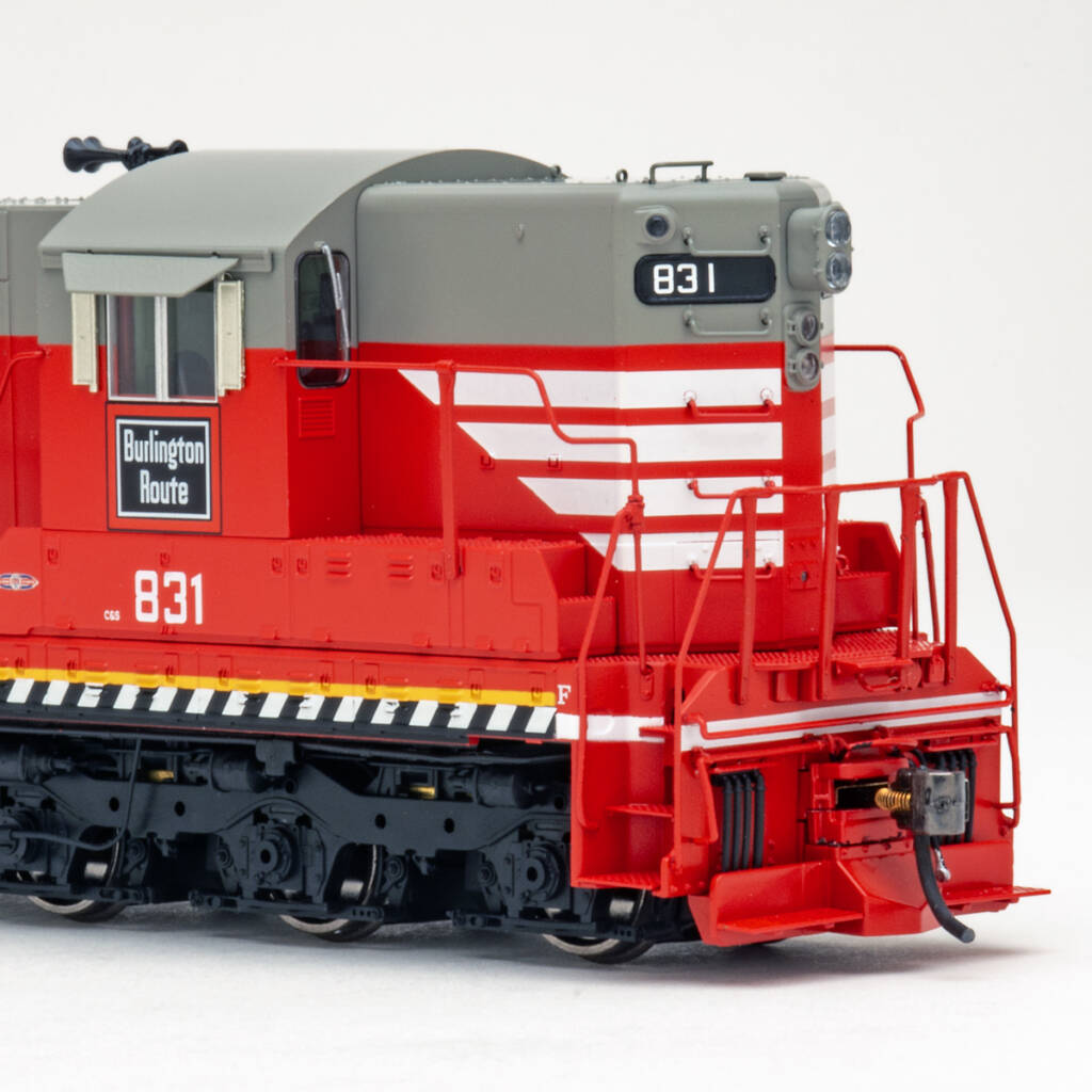 Color photo showing nose of HO scale diesel locomotive painted red and gray with white, yellow, and black graphics on white background.